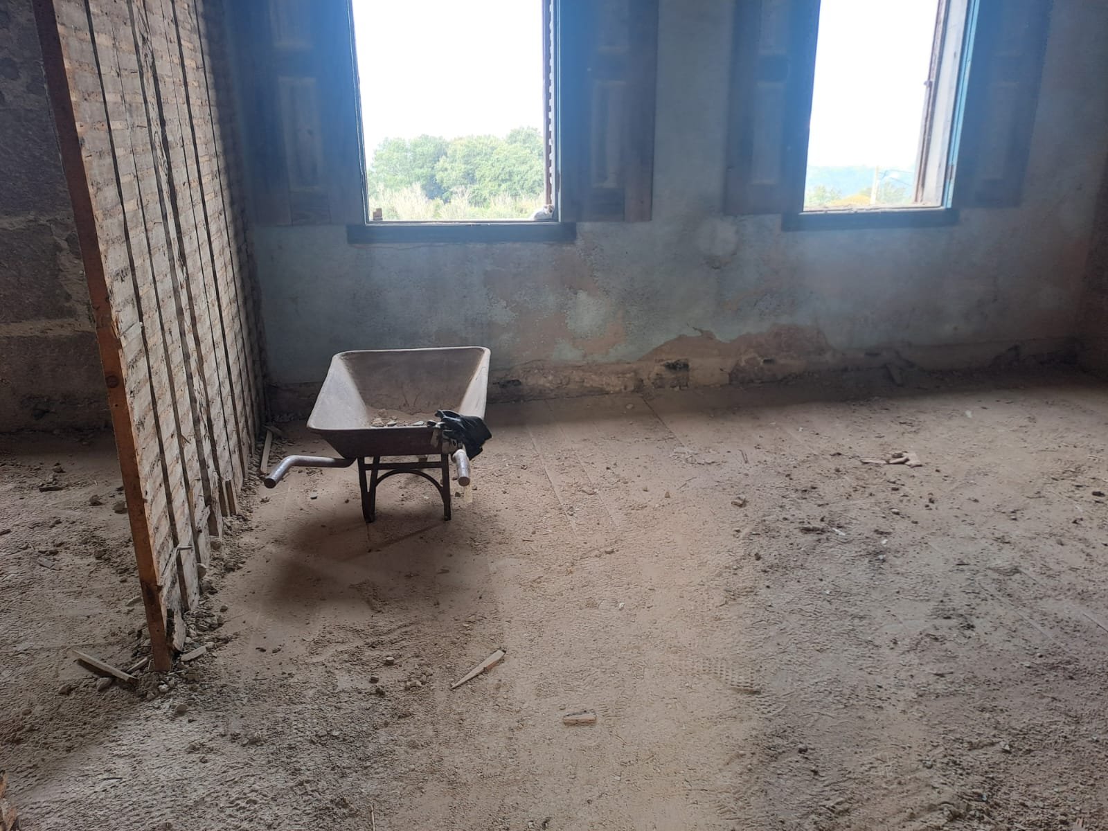 A wheelbarrow parked in a gutted room, exposed lath on the wall