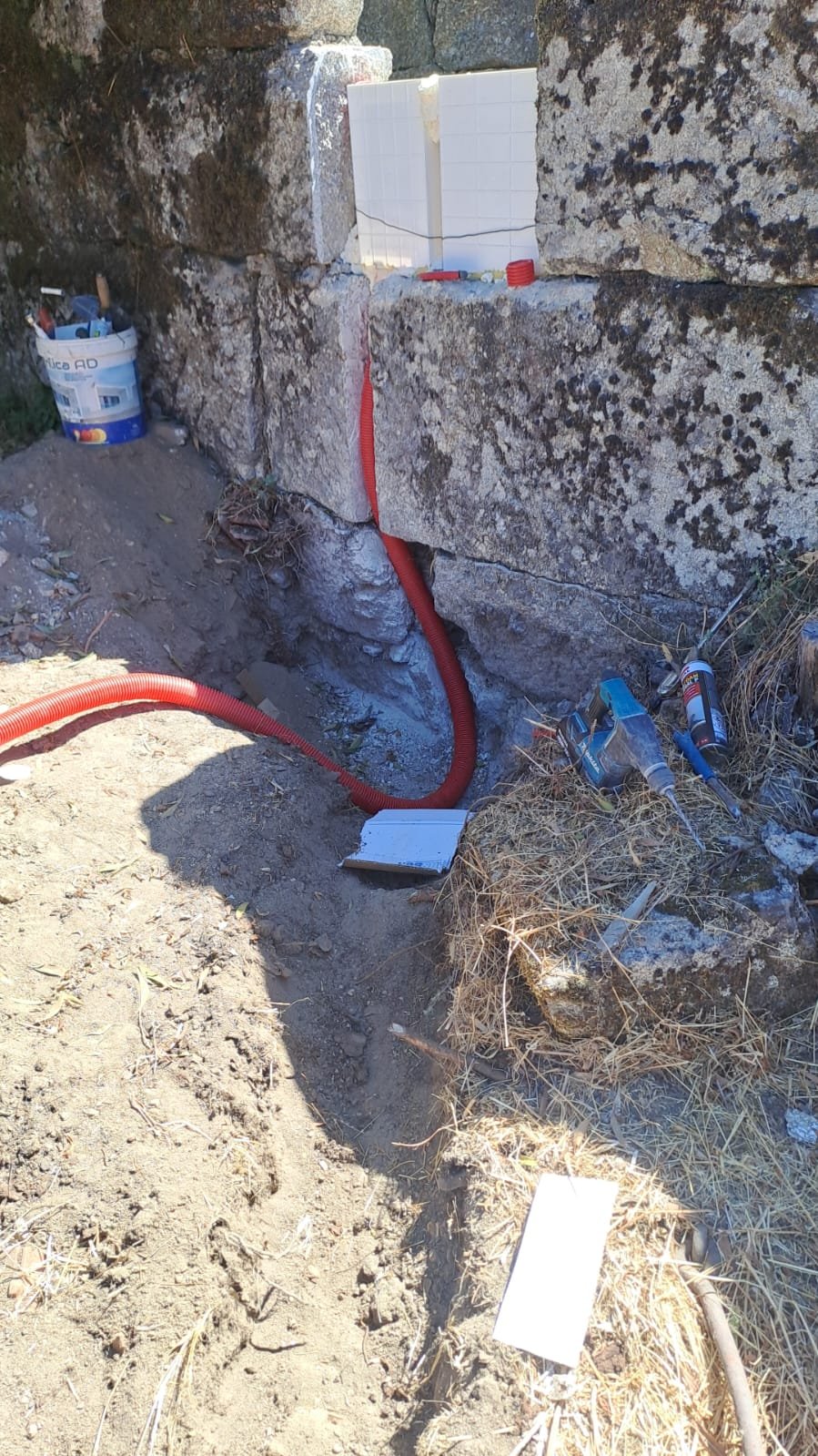 Red electrical conduit entering the stone wall at the base of the property